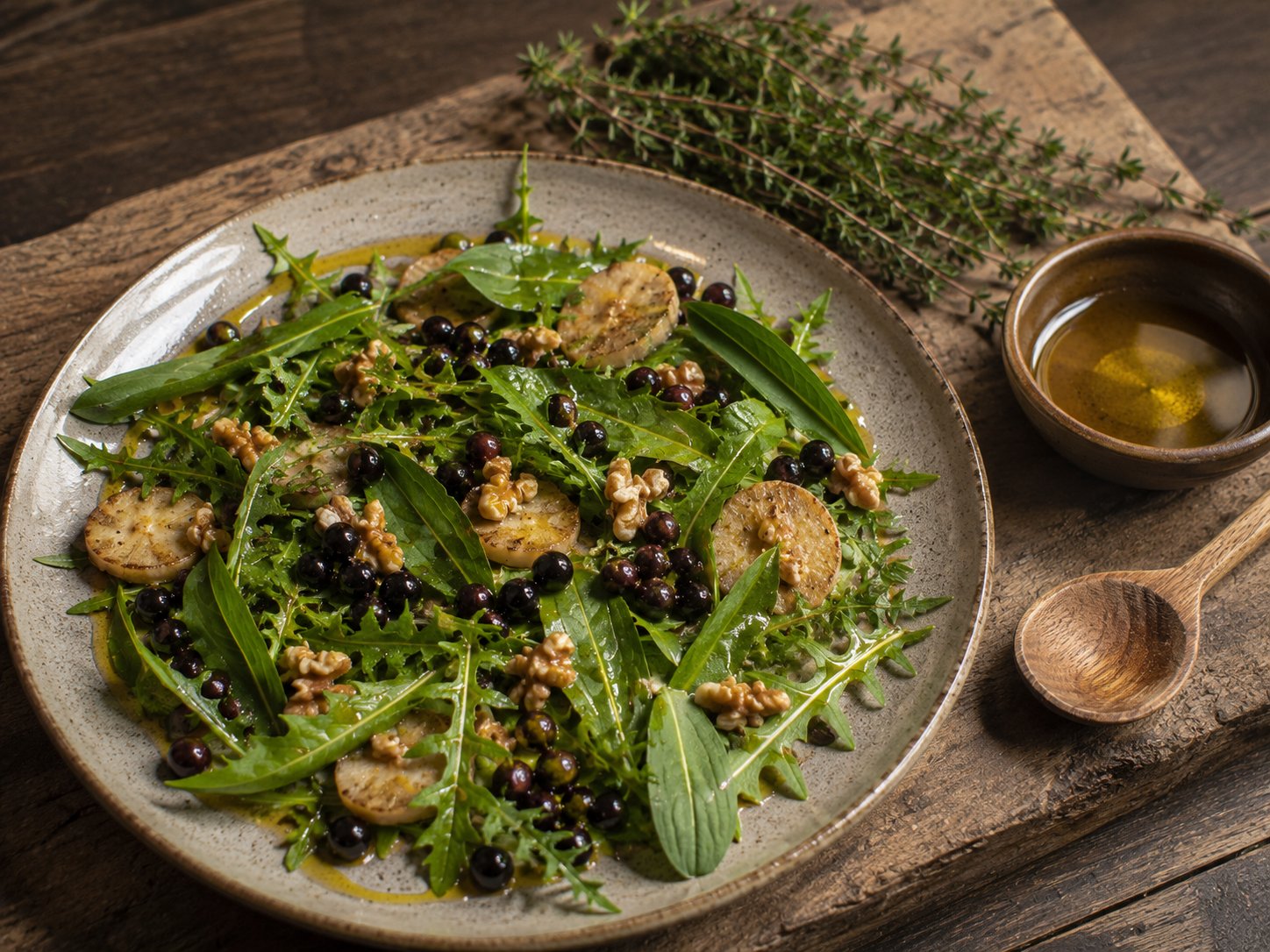 Assiette anti-inflammatoire composée de feuilles sauvages vertes, baies violettes, noix, huile dorée et racines — présentation soignée sur bois